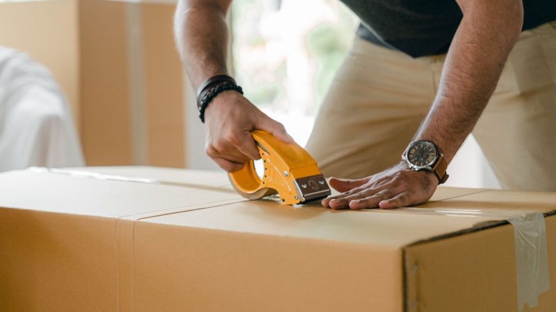 Crop unrecognizable young male in casual clothes packing cardboard box and sealing with scotch tape — Before You Decide To St