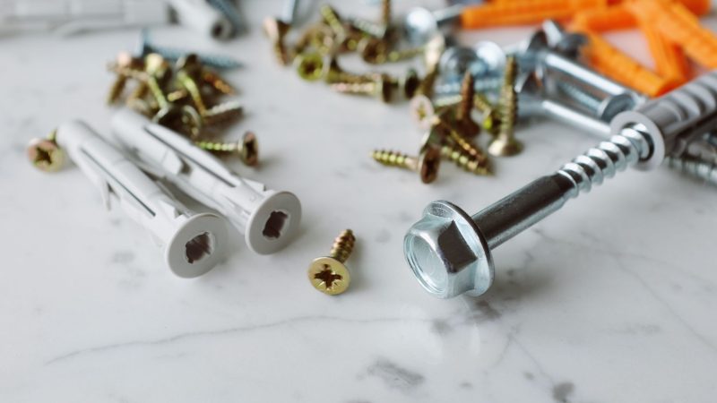 Closeup view of various multicolored plastic dowels with metal screws of different sizes placed on white marble table in mode