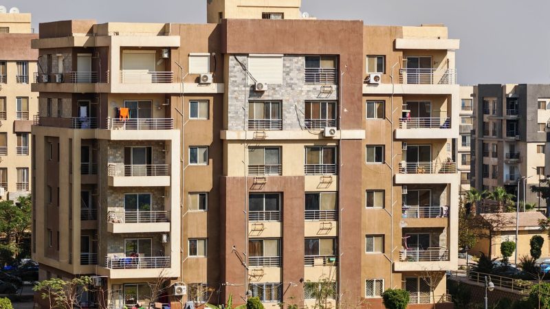 A sunny urban scene of a modern apartment building exterior with balconies and greenery. — Setting the factors for a realtor