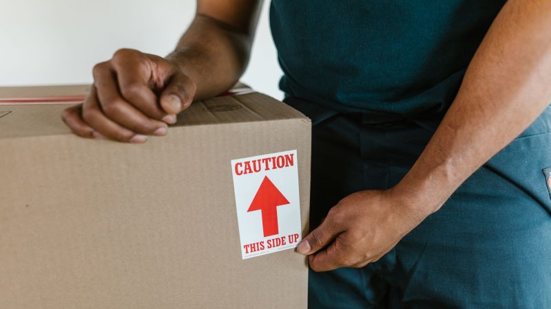 A person handling a moving box with a 'caution this side up' label indoors. — Ways to get washboard midsection both at home a