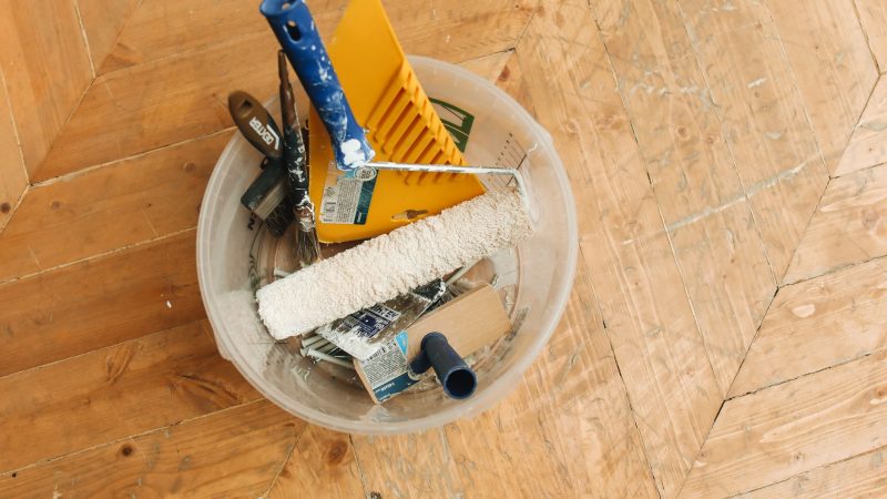 A collection of home renovation tools in a bucket on a wooden floor, ready for a painting project. — White-colored Bear Lake 